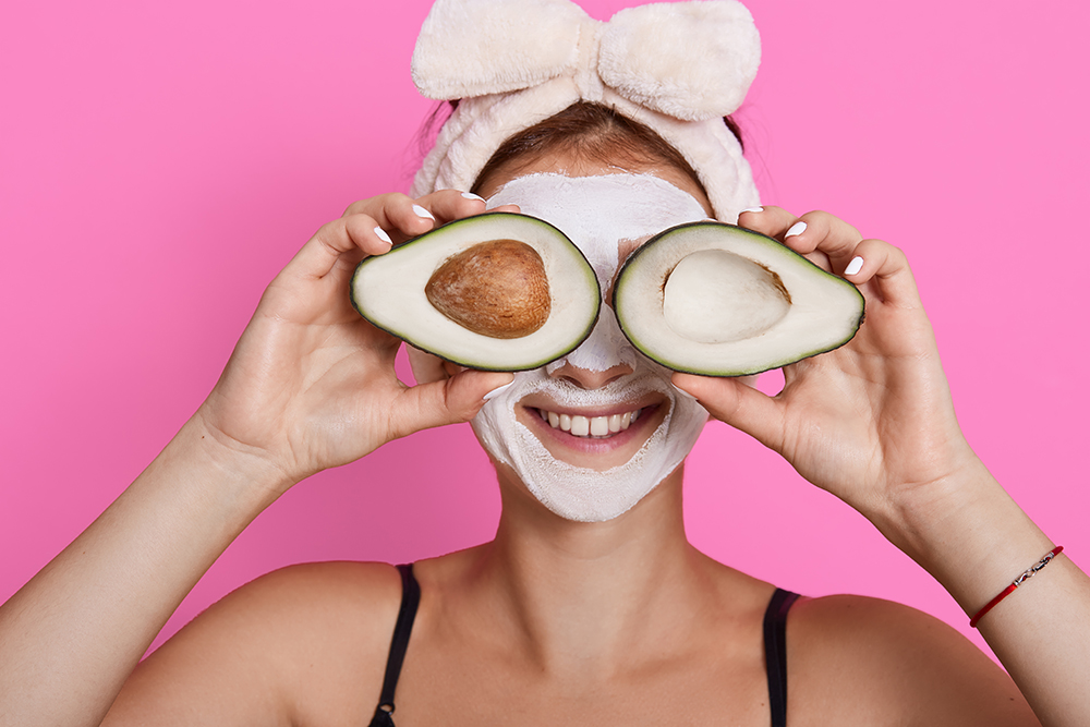 Closeup portrait of woman 20s with perfect skin holding avocado against her eyes isolated over pink background, healthcare, cosmetic procedures at home.