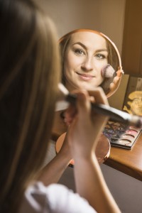 close-up-of-beautiful-woman-with-hand-mirror-applying-blusher-on-her-face