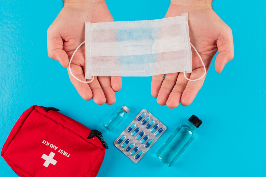 Top view first aid kit in hands with mask, vial, pills and bottle on cyan blue background. horizontal